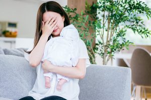 赤ちゃんを抱っこしながら、体の不調を感じている女性