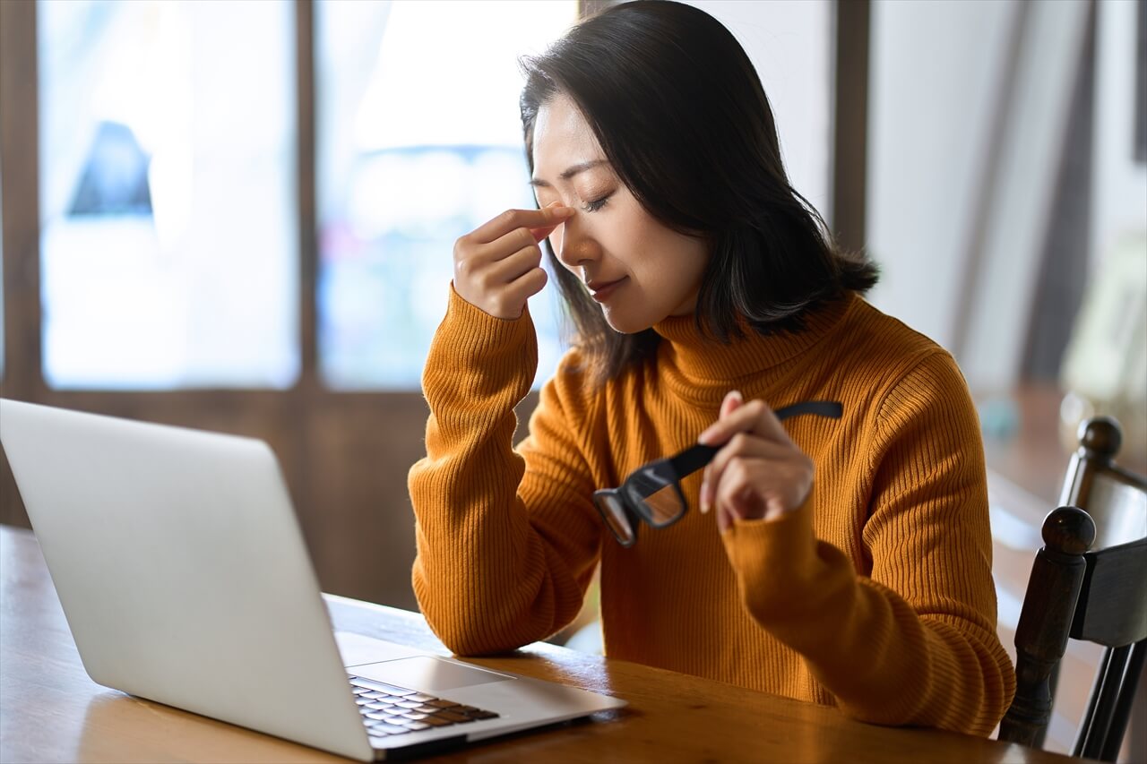 眼精疲労で目を押さえるデスクワーク中の女性