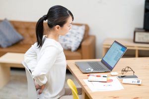 デスクワークをしている、腰の痛みを気にしている女性